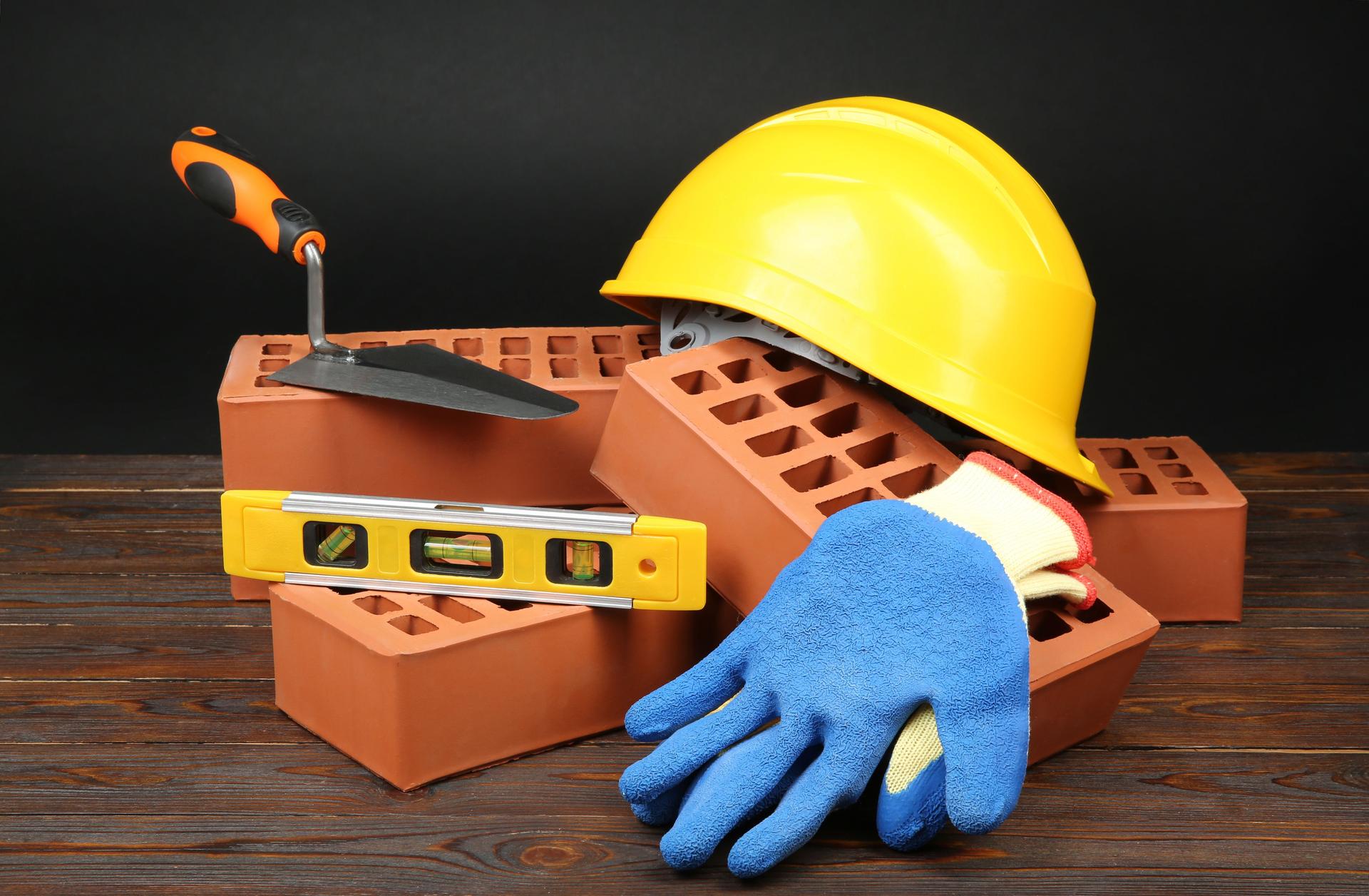 Red bricks, different construction tools and safety equipment on wooden table