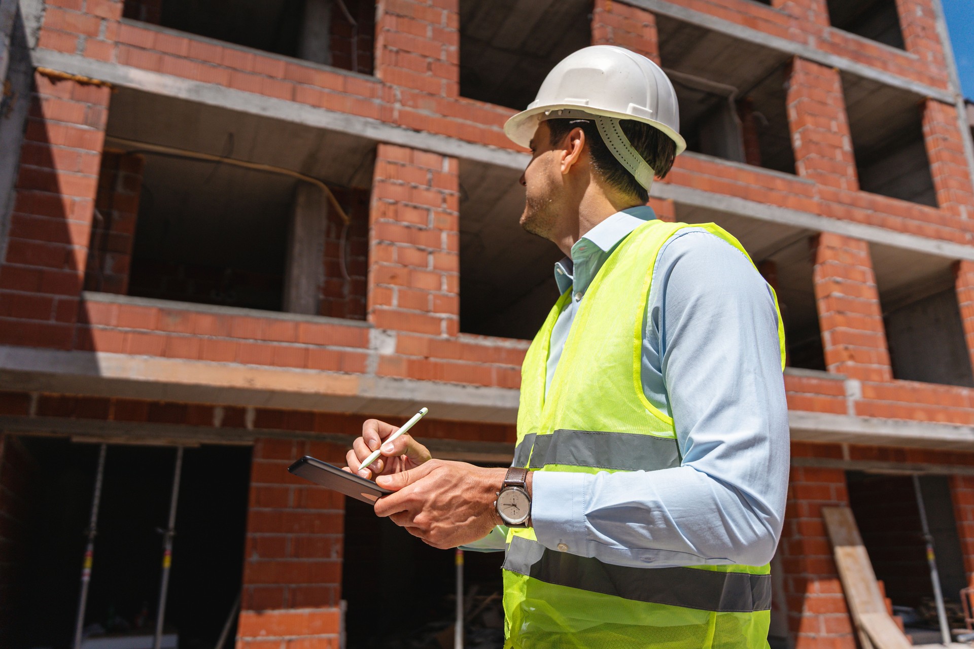Engineer Inspecting a Brick Building at a Construction Site with a Notepad